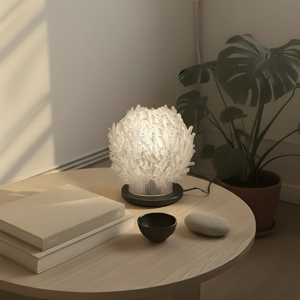 White textured table lamp on a wooden table with books and a plant in a room.